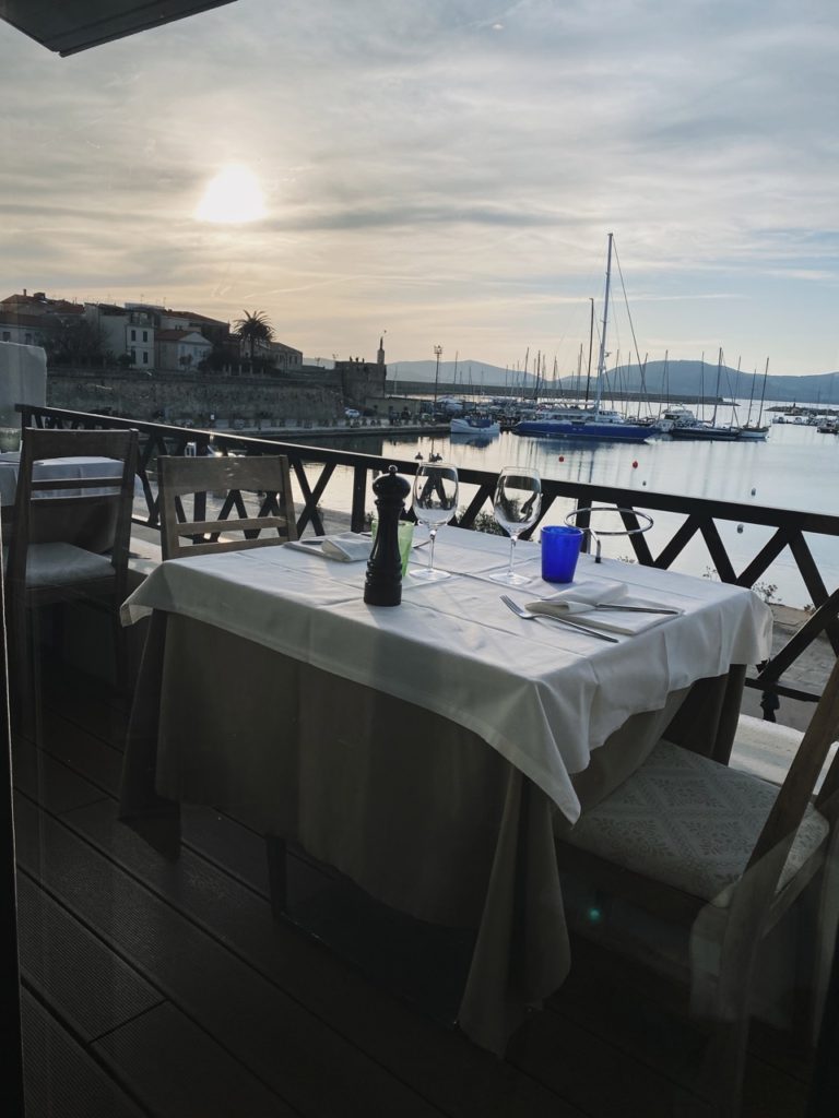 Set table on a balcony overlooking the Alghero harbor at sunset