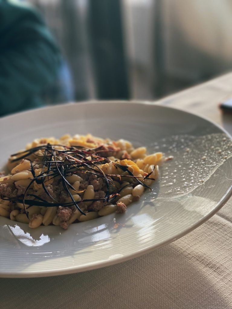 A plate of pasta topped with meat and dark herbs in Alghero