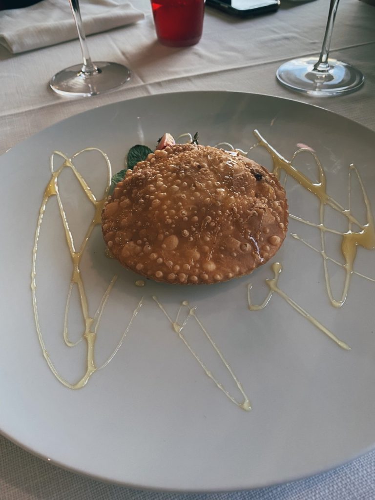 Fried pastry drizzled with honey on a white plate in Alghero