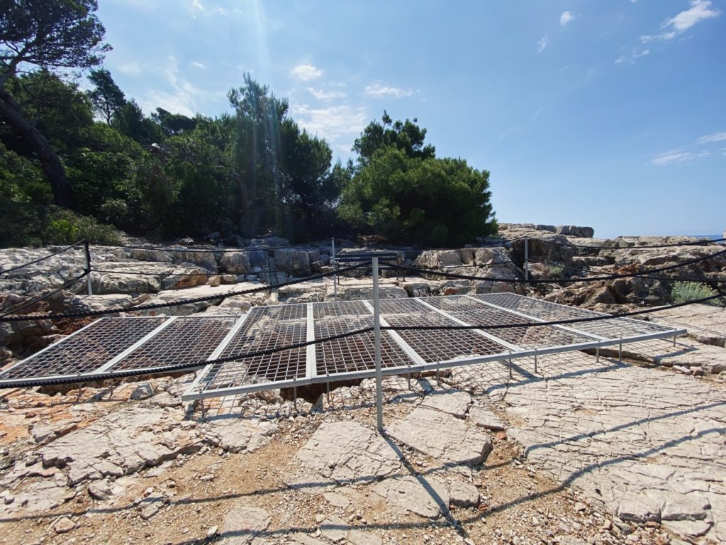 Metal grates cover a rocky opening on Lokrum Island surrounded by trees