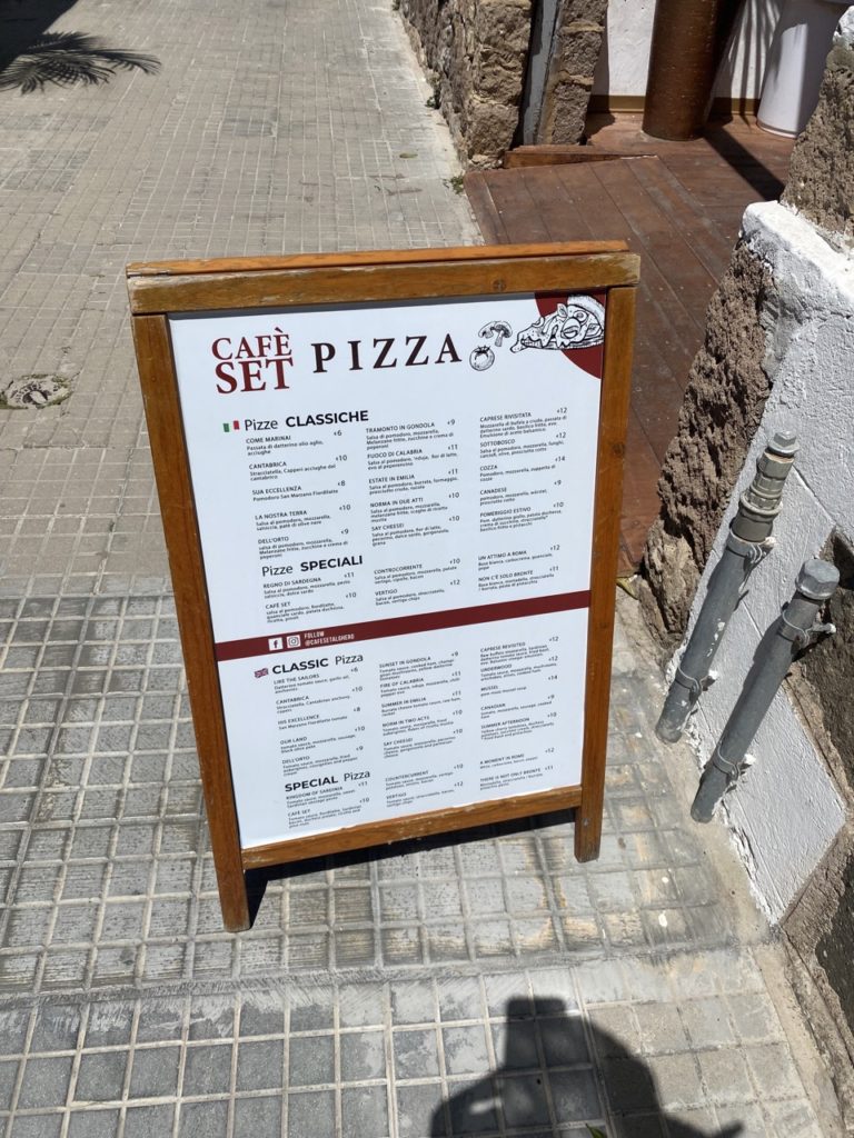 A wooden sandwich board menu for a pizza restaurant stands on a sidewalk