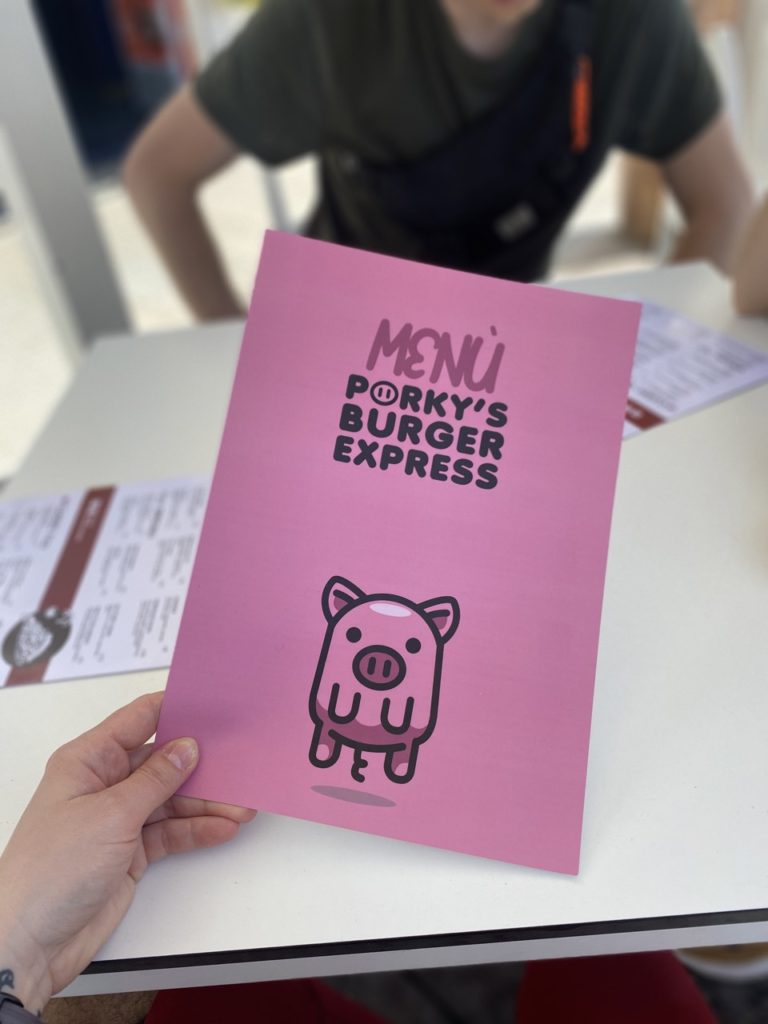 Hand holding a pink Porky's Burger Express menu at a table