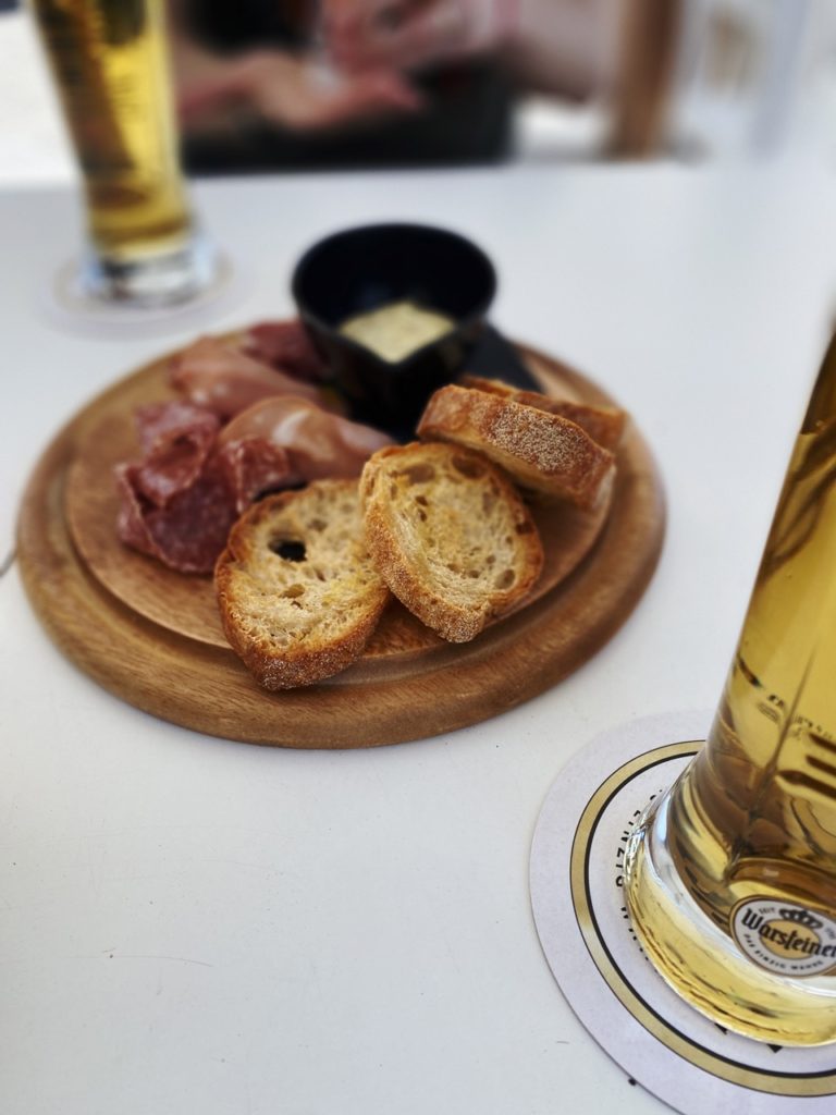 Wooden board with sliced bread and cured meats served with glasses of beer
