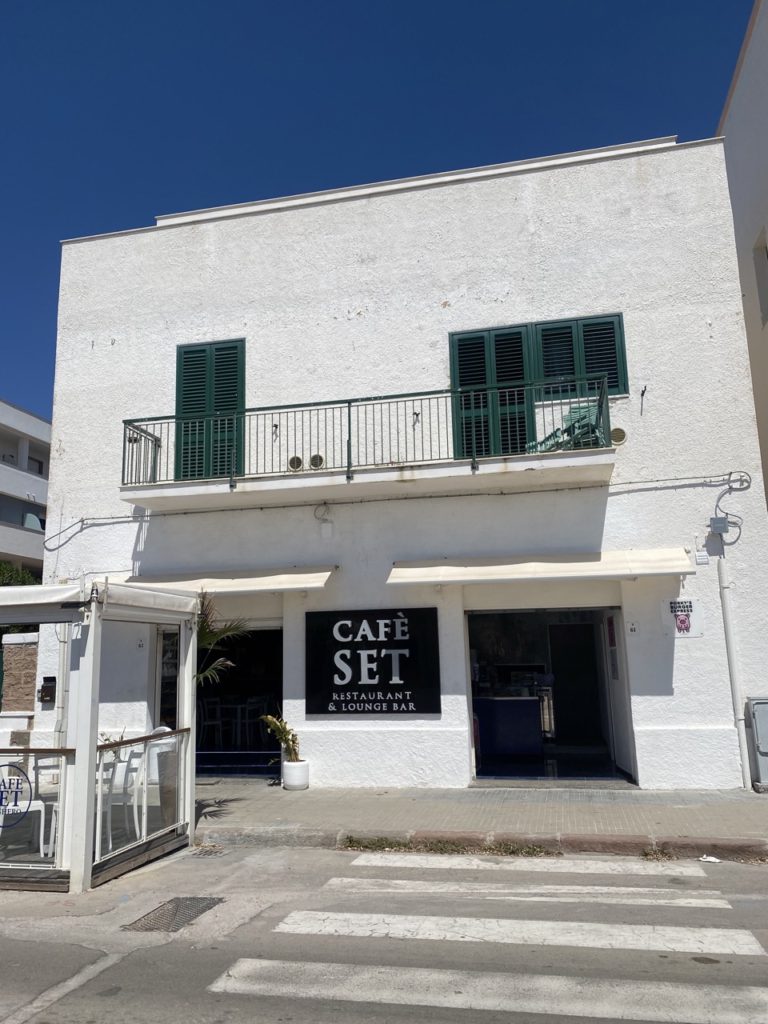 White building with a balcony and the Cafe Set restaurant sign in Alghero