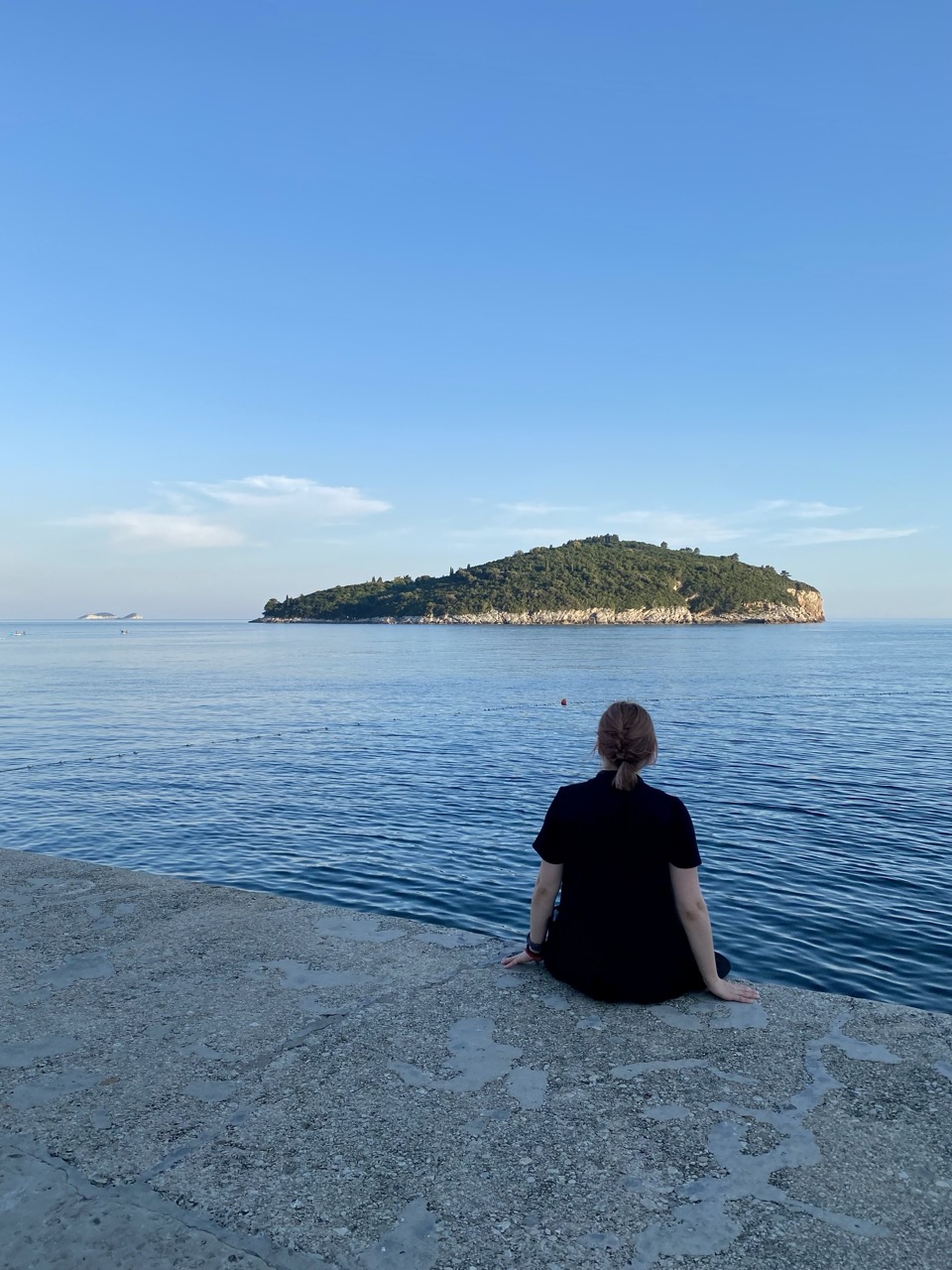 A person sitting on a stone pier looking out at Lokrum Island in Dubrovnik