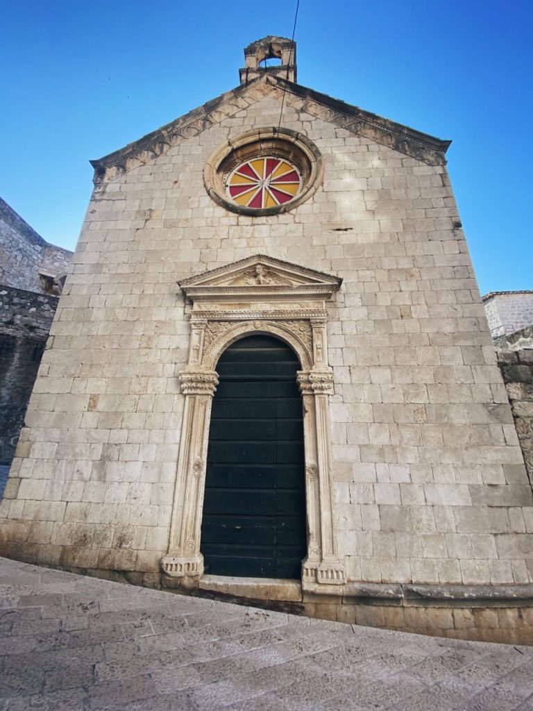 Stone facade of a historic Dubrovnik church with a colorful circular window