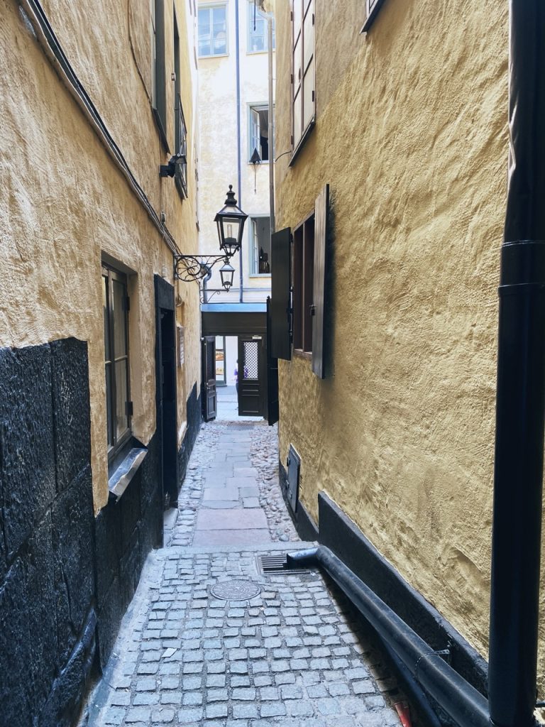 Narrow cobblestone alleyway between tall yellow buildings in Stockholm