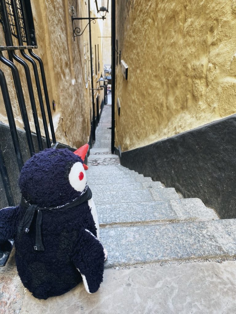 A plush penguin sits at the top of a narrow Stockholm alleyway staircase