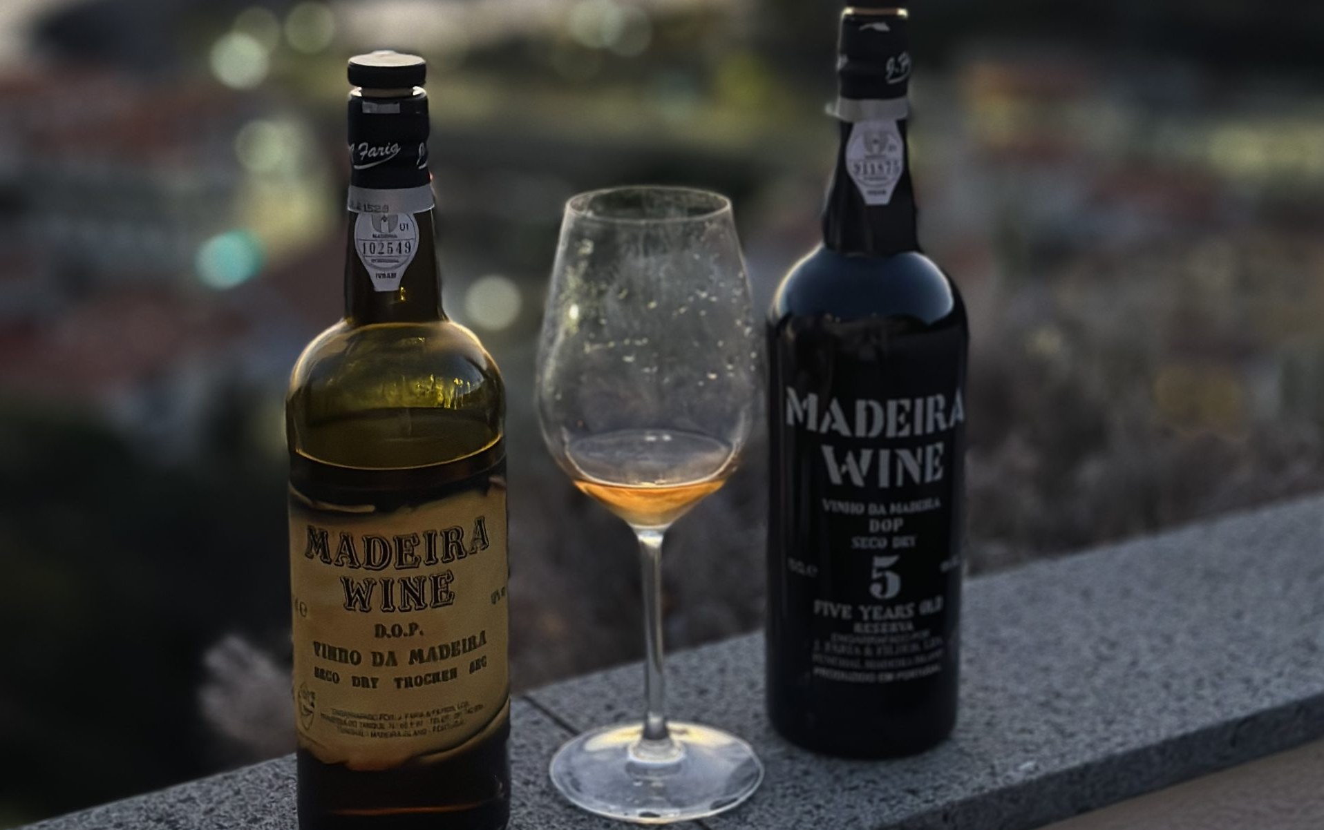 Two bottles of Madeira wine and a glass on a stone ledge at dusk, Madeira
