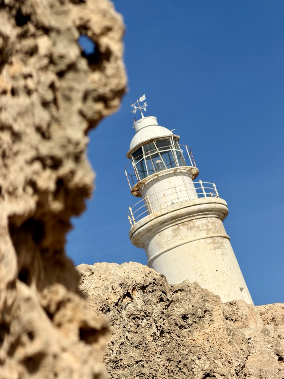 White lighthouse rising behind jagged rocks in Paphos Archaeological Park