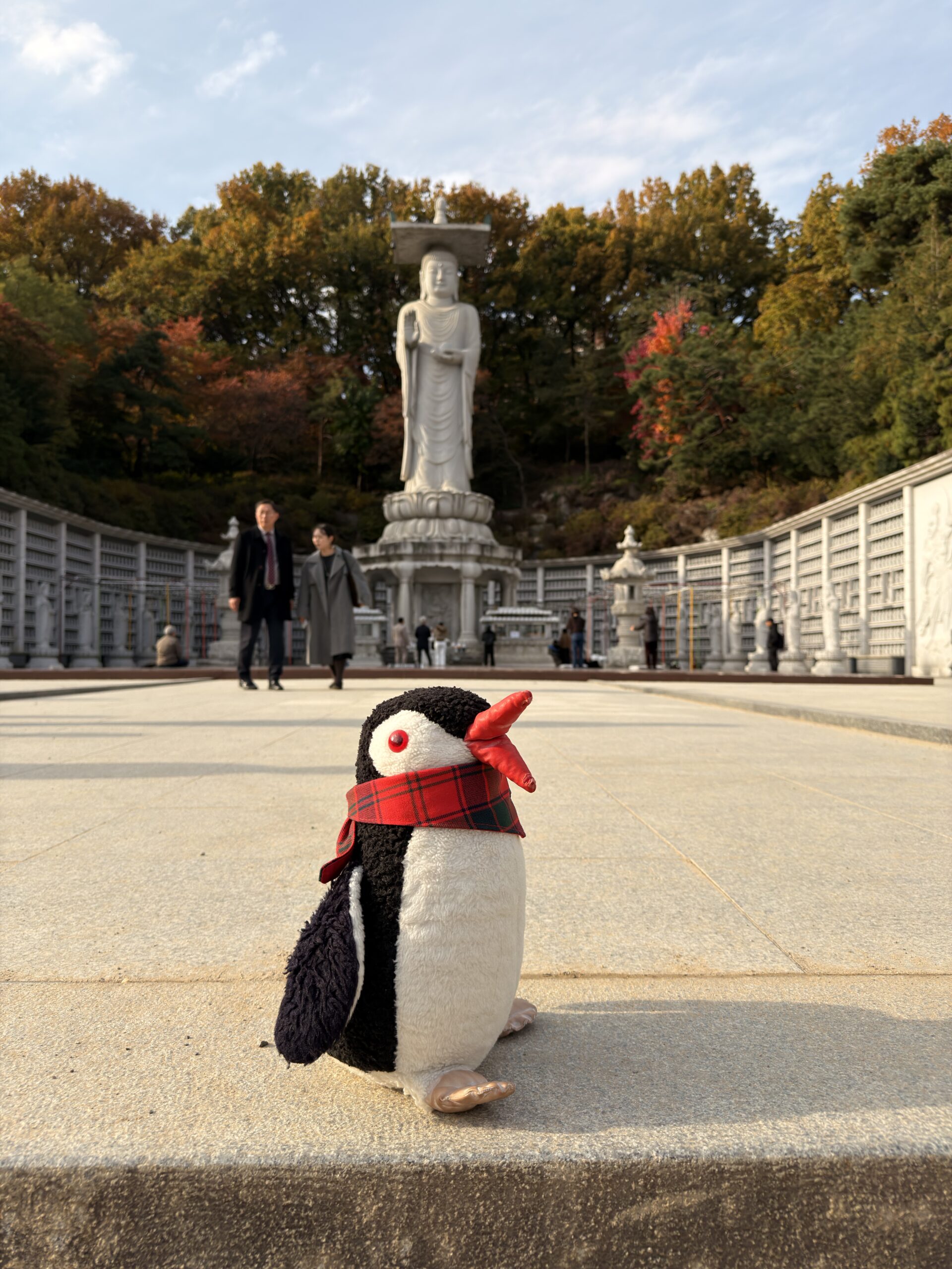 A stuffed penguin toy stands in front of a large stone Buddha statue