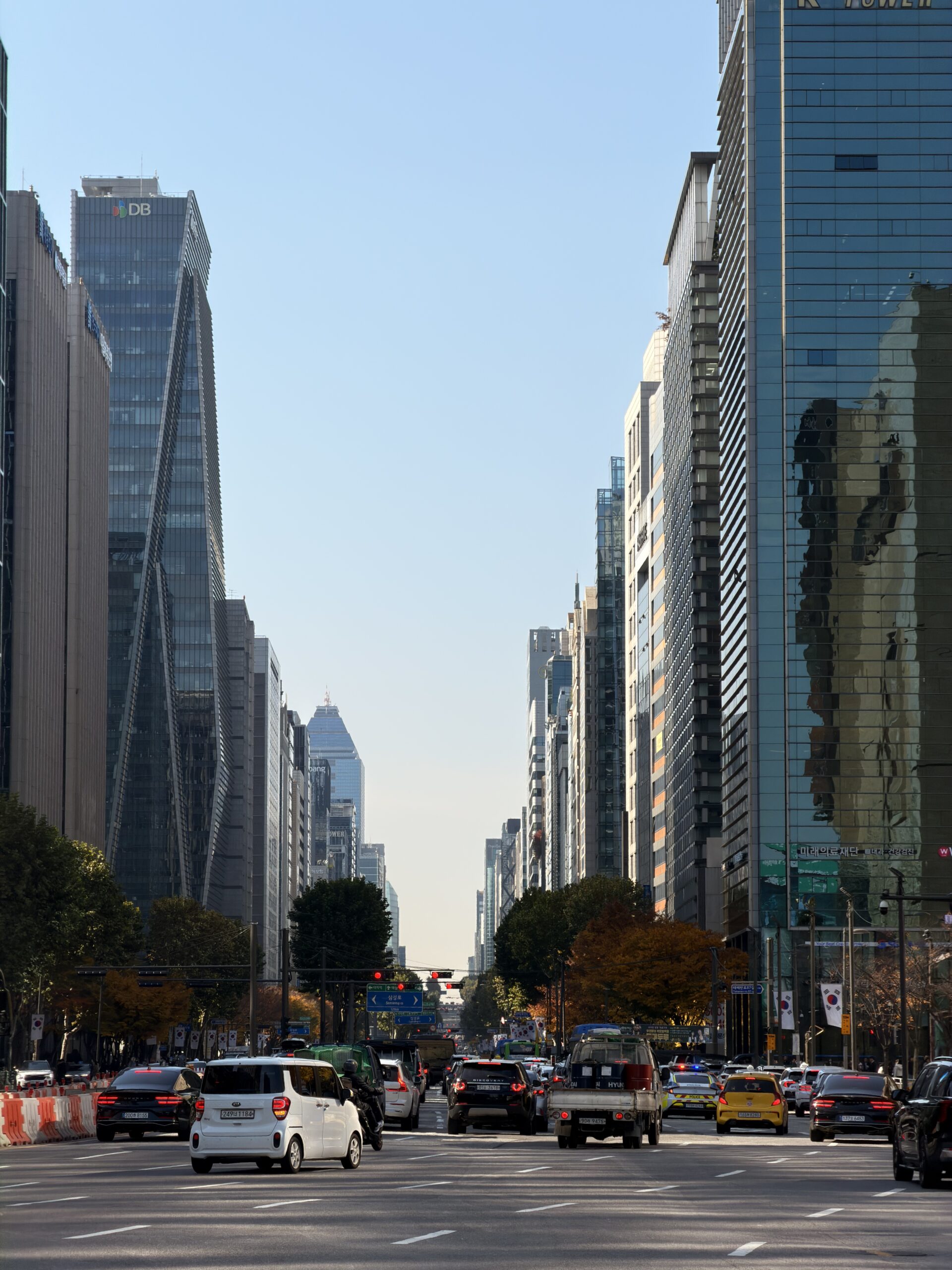 Cars drive down a wide street lined with tall skyscrapers in Seoul