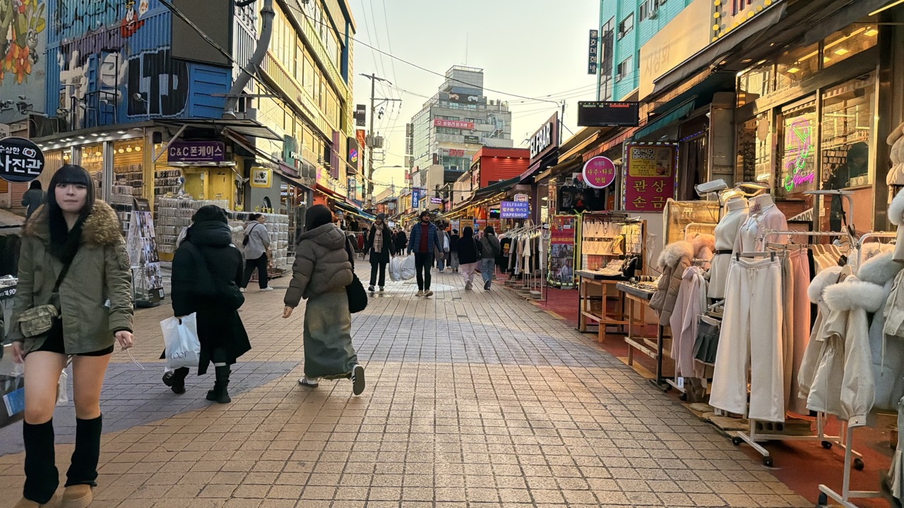 People walk along a vibrant shopping street in Seoul lined with colorful storefronts