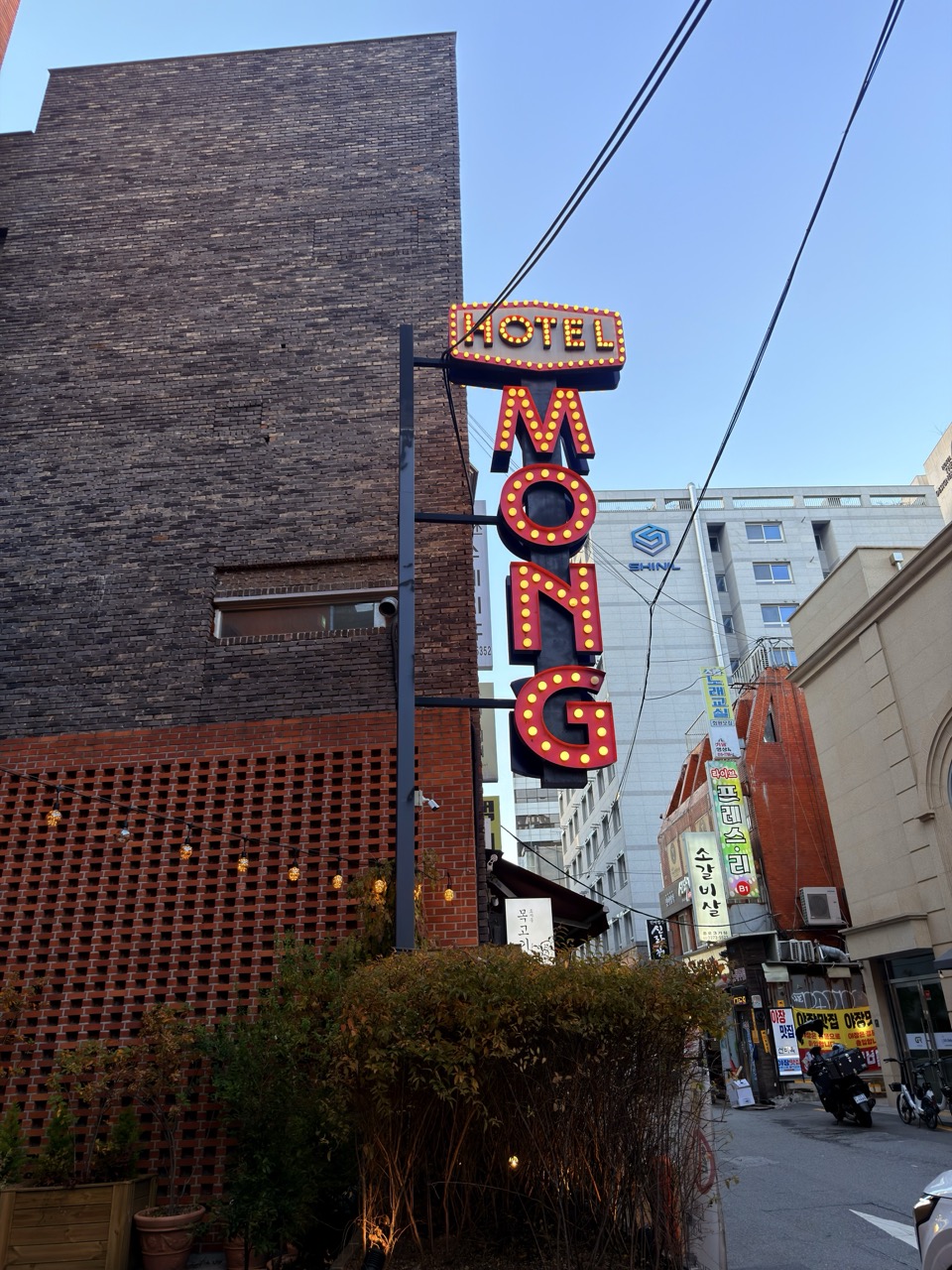 Illuminated Hotel Mong sign hanging above a Seoul street with brick buildings