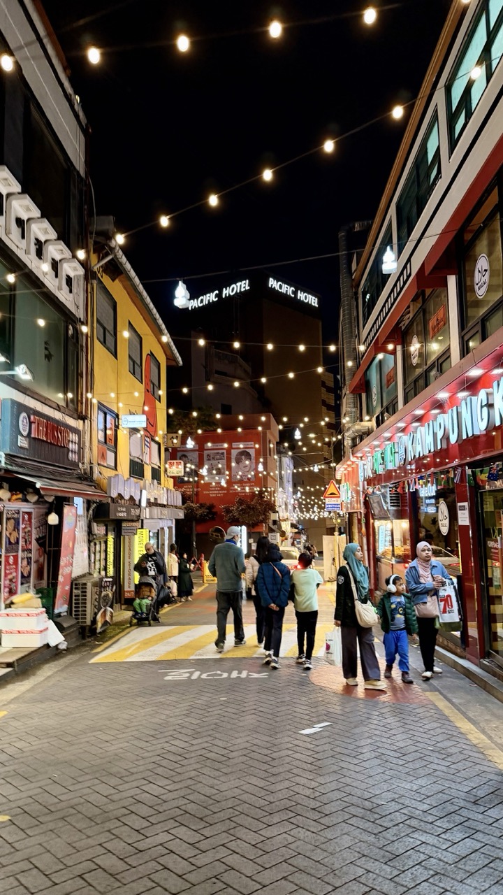 People walk down a brightly lit street in Seoul at night