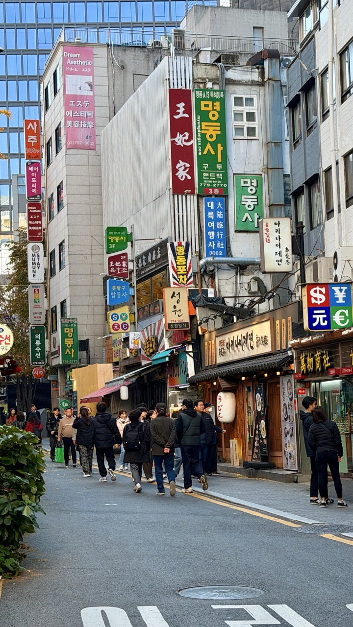 People walk along a narrow Seoul street lined with colorful business signs