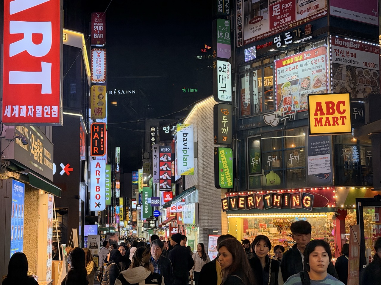A crowded street at night in Seoul filled with bright neon shop signs