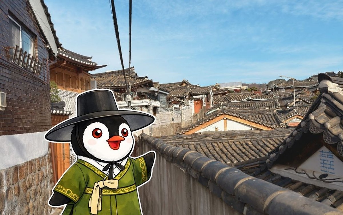 Miško the toy penguin wearing a traditional hat and green robe overlooking a Hanok village in Seoul