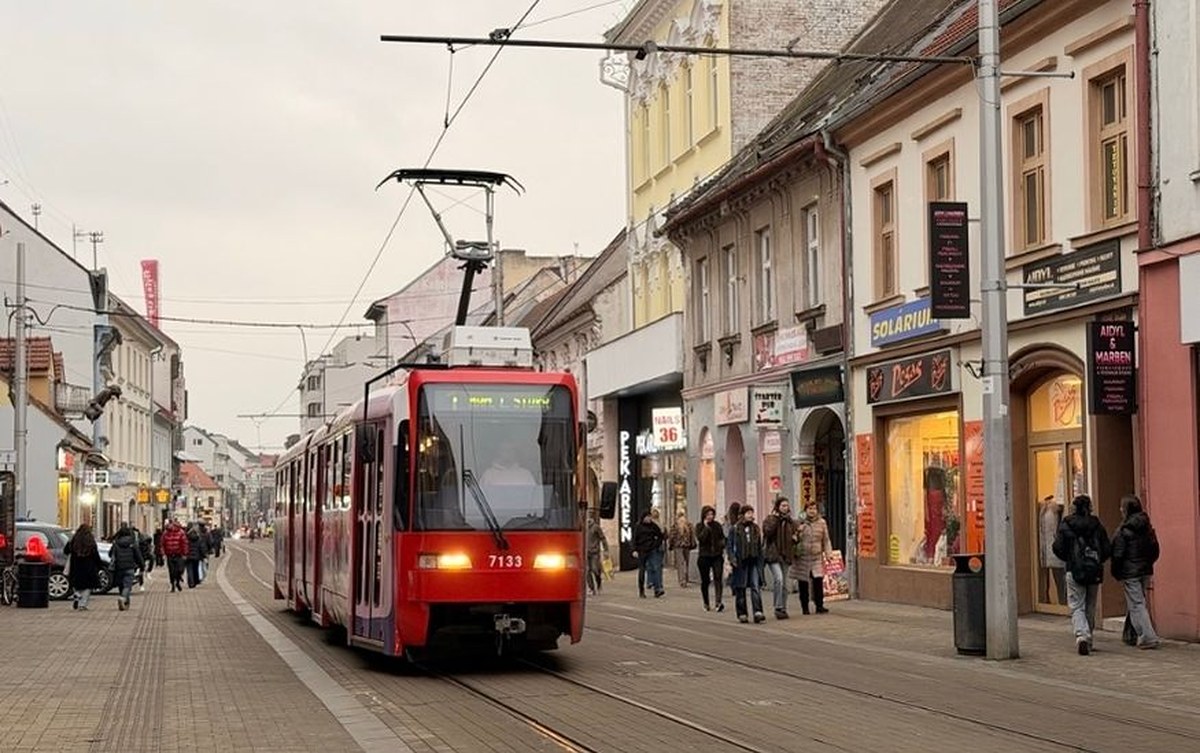 A red tram moving through a street in Bratislava Public Transport Guide with pedestrians walking on the sidewalk