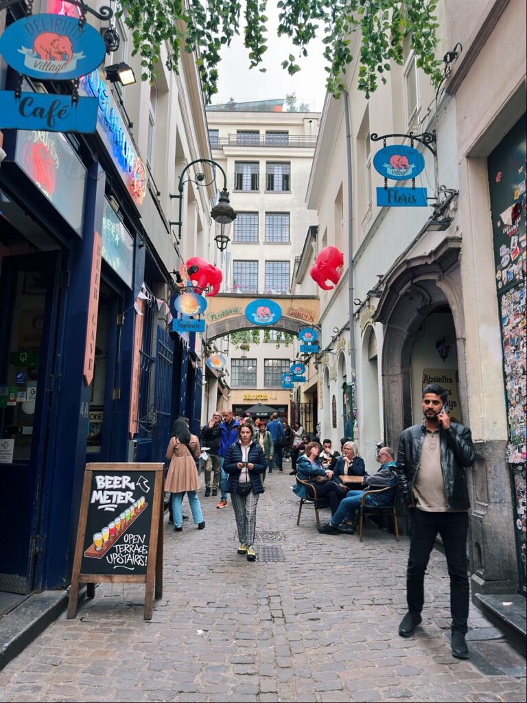 People walk through a narrow cobblestone alleyway in Brussels lined with bars