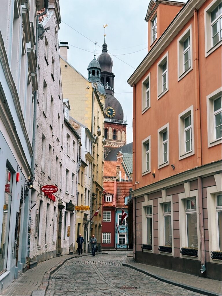 Riga city street with historic building facades, windows and a sidewalk, featuring a visible sign