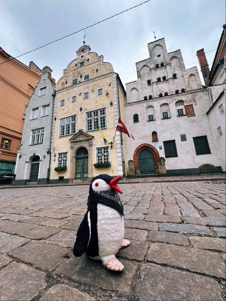 A small knitted penguin toy rests on a map of Latvia