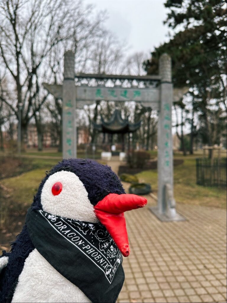 Miško the knitted penguin plush standing near a sign