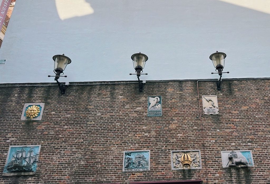 Three street lamps above decorative plaques on a brick wall in Amsterdam