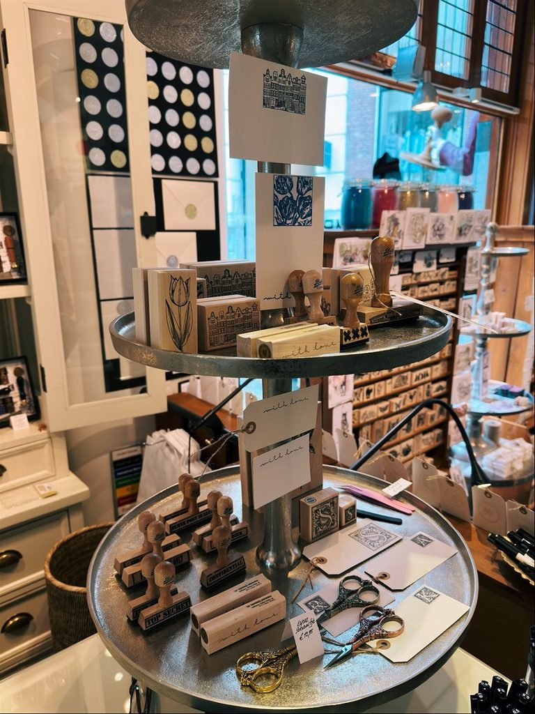Wooden rubber stamps featuring tulips and canal houses are arranged on a tiered metal stand with small scissors and tags reading with love