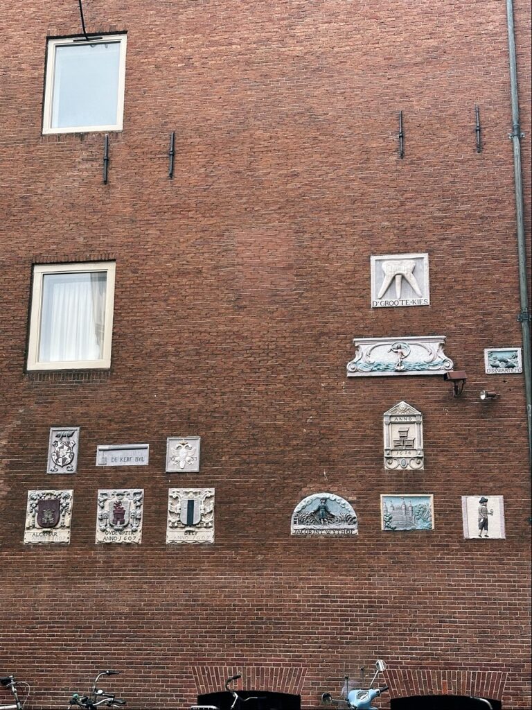 A brick wall in Amsterdam with decorative plaques and a window with white curtains