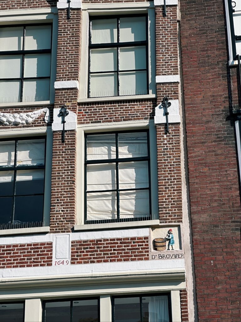 Red brick Amsterdam house facade with tall windows, lifting hooks, the date 1649 and a tile reading D' BROVVER