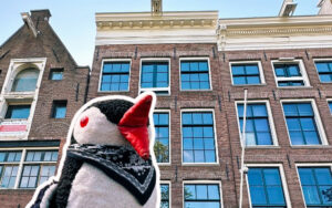 Miško the knitted penguin looks up at the brick facade of the Anne Frank House in Amsterdam