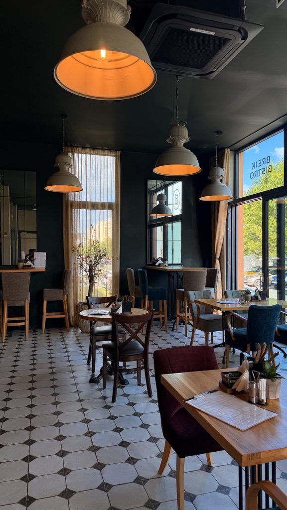 Interior of Brejk Bistro Prešov with dark walls, geometric floor tiles, wooden tables, velvet chairs, and hanging lights