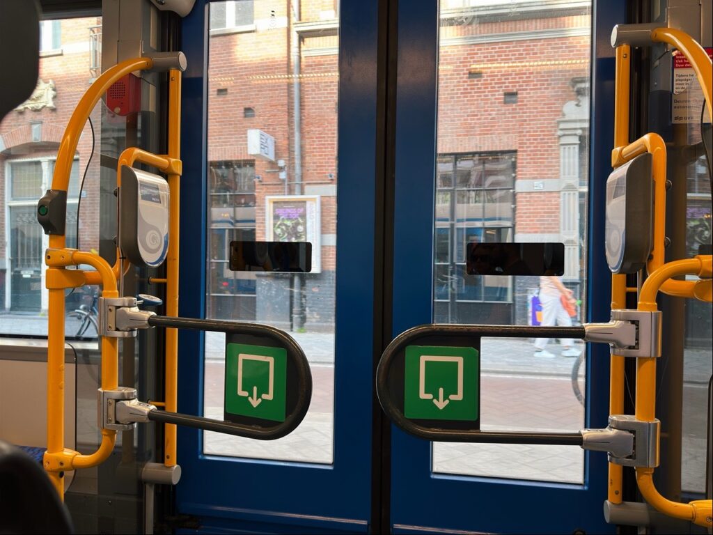 Blue doors with yellow handrails and green card reader stickers inside a tram in Amsterdam