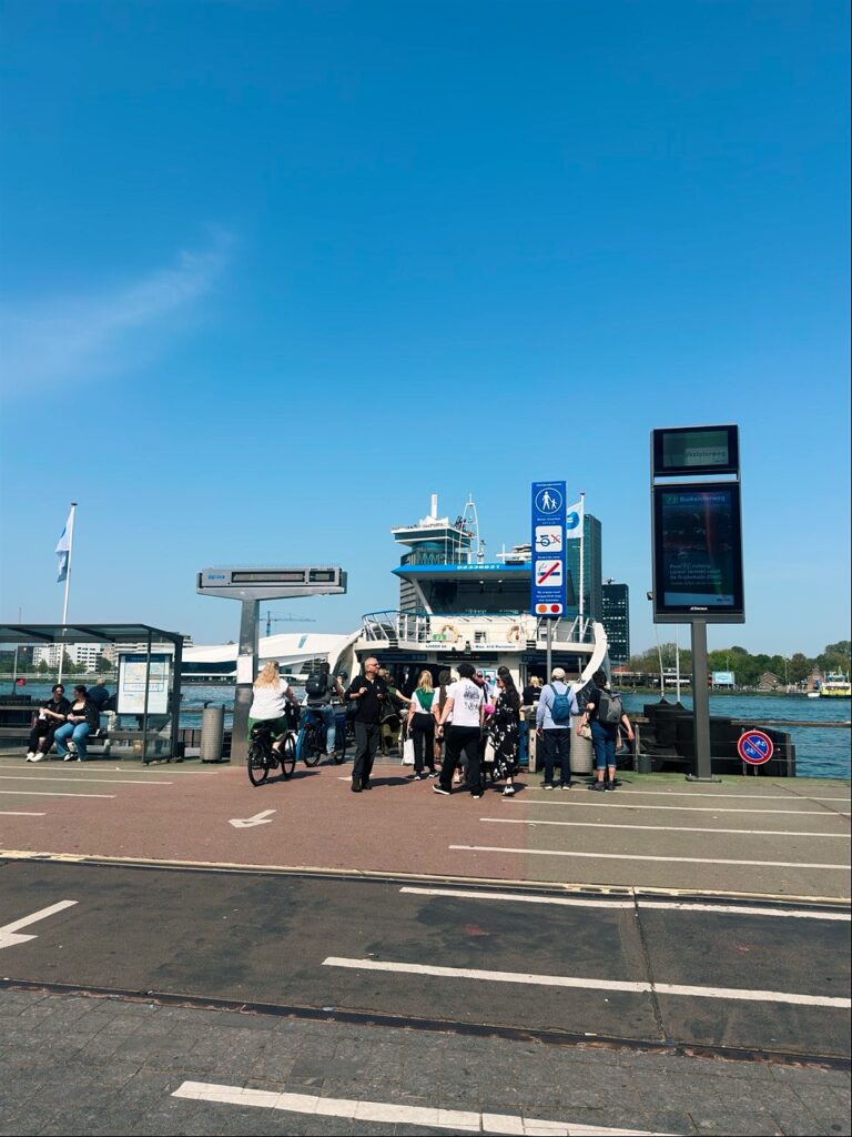 Cyclists and pedestrians waiting on a sunny pier to board a ferry in Amsterdam