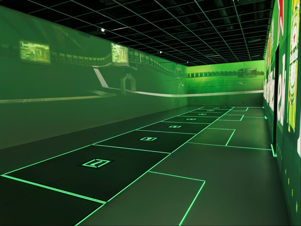 Green lit room with floor squares numbered one to seven and wall projections at the Heineken Experience Amsterdam