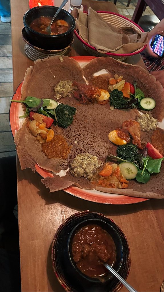A large platter of injera bread topped with various stews and vegetables sits on a wooden table at Lalibela Amsterdam