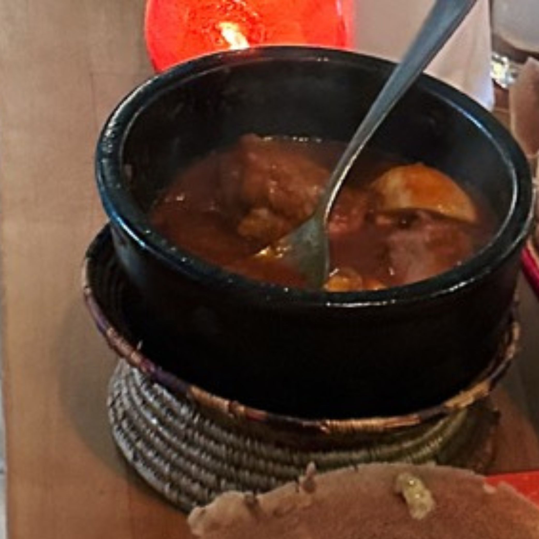 A black bowl of stew with a spoon inside and a piece of flatbread in the foreground at Lalibela Amsterdam