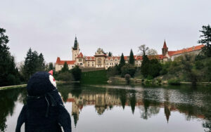 Miško the knitted penguin gazes at the castle and its reflection in the pond at Průhonice Park