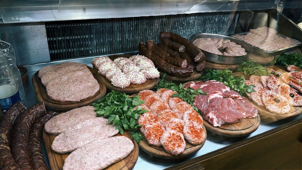 Assorted raw meats including sausages, patties, and steaks displayed on wooden boards at Restaurant Familjar Pashtriku Prizren