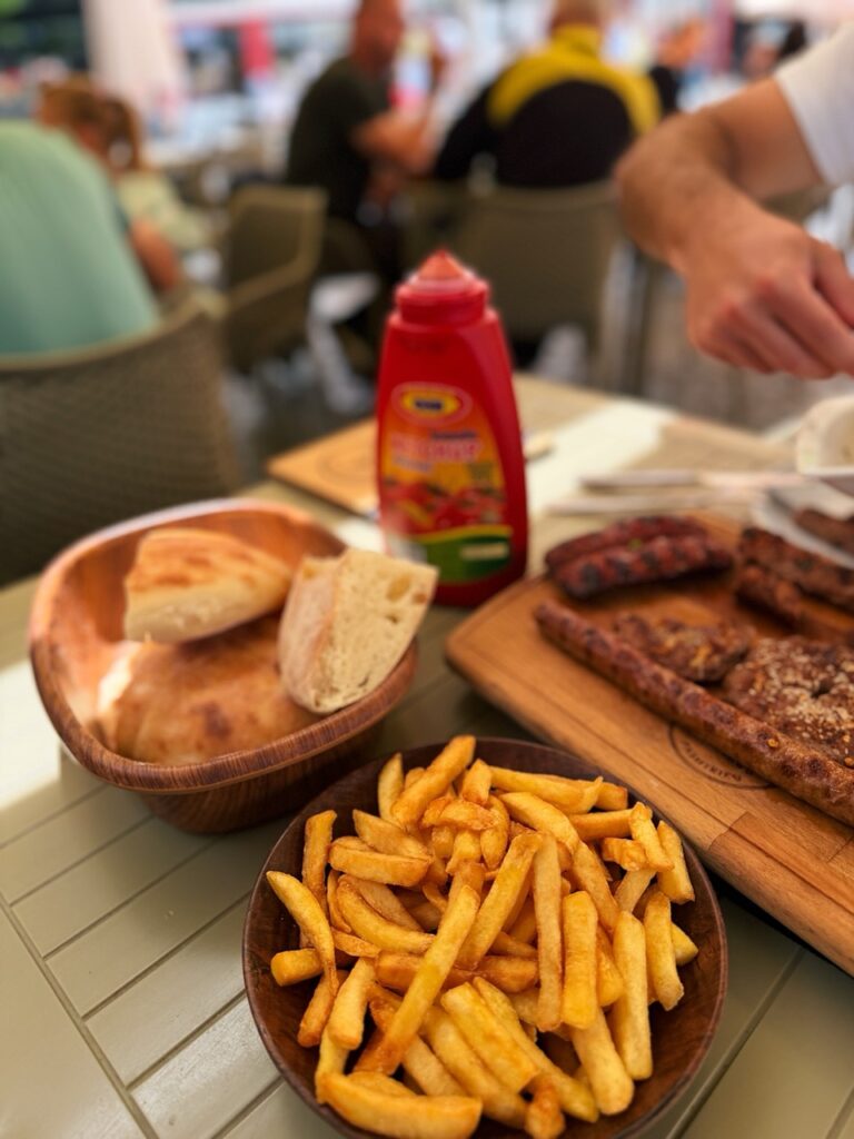 A table with fries bread grilled meats and a ketchup bottle at Restaurant Familjar Pashtriku Prizren Kosovo