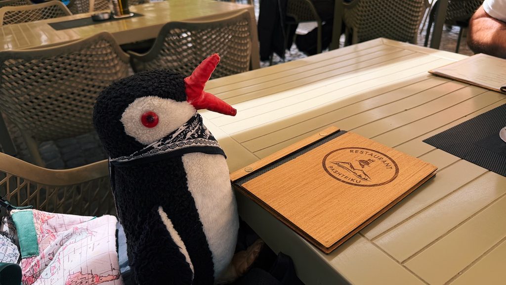 Miško sits at a table with a wooden menu board for Restaurant Familjar Pashtriku Prizren