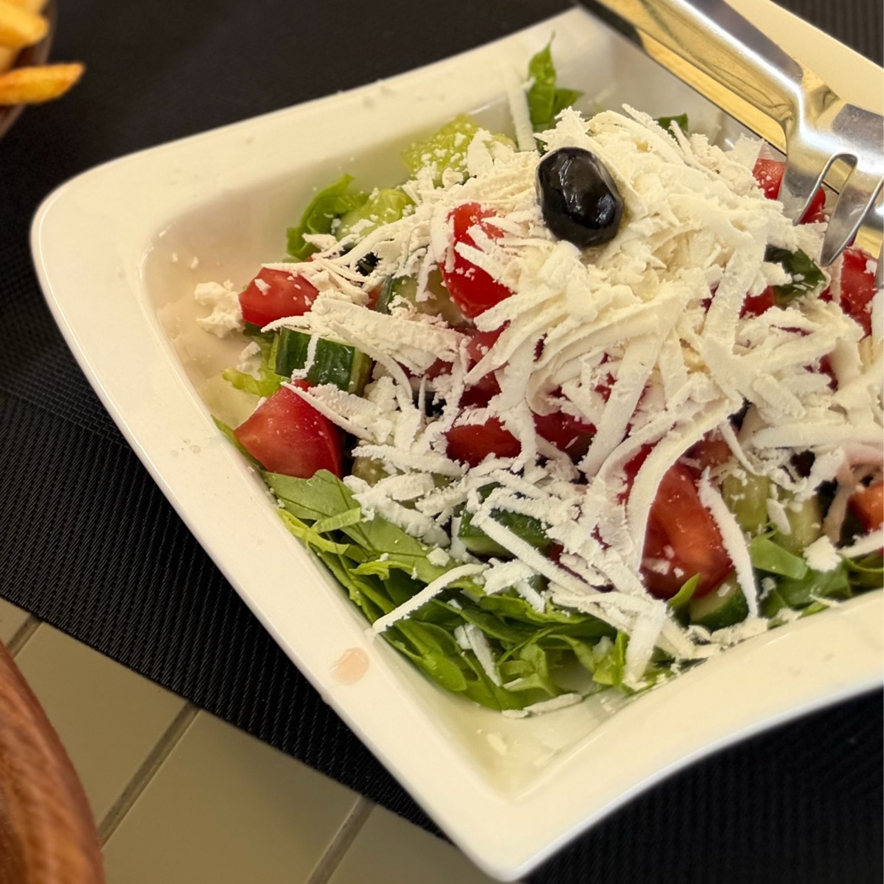 Salad with lettuce, tomatoes, cucumbers, and shredded cheese in a white bowl at Restaurant Familjar Pashtriku Prizren