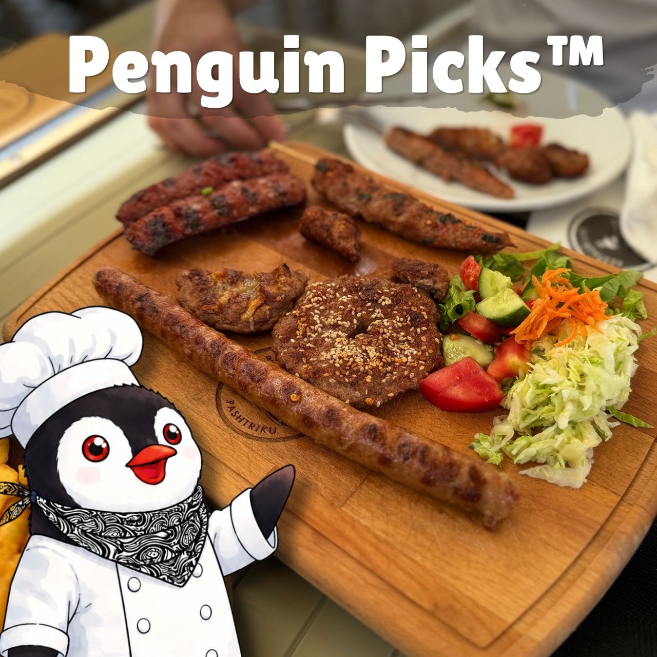 Miško the knitted toy penguin stands next to a wooden board filled with grilled meats and fresh salad at Restaurant Familjar Pashtriku Prizren Kosovo