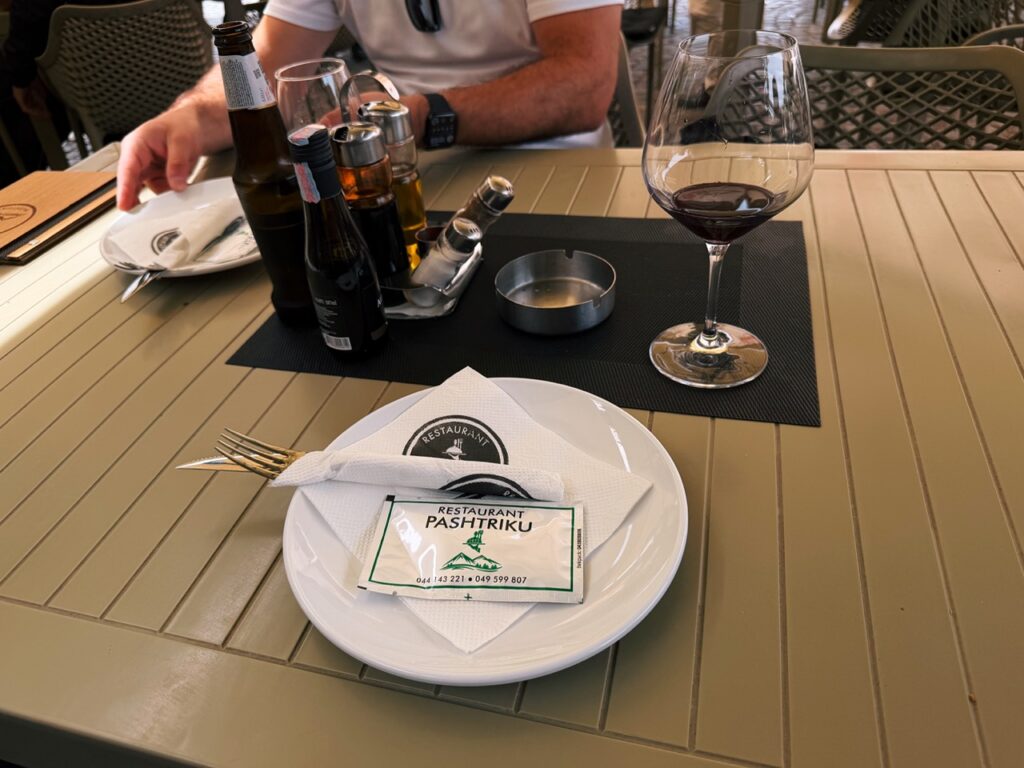 A table setting at Restaurant Familjar Pashtriku Prizren with plates bottles and a glass of wine