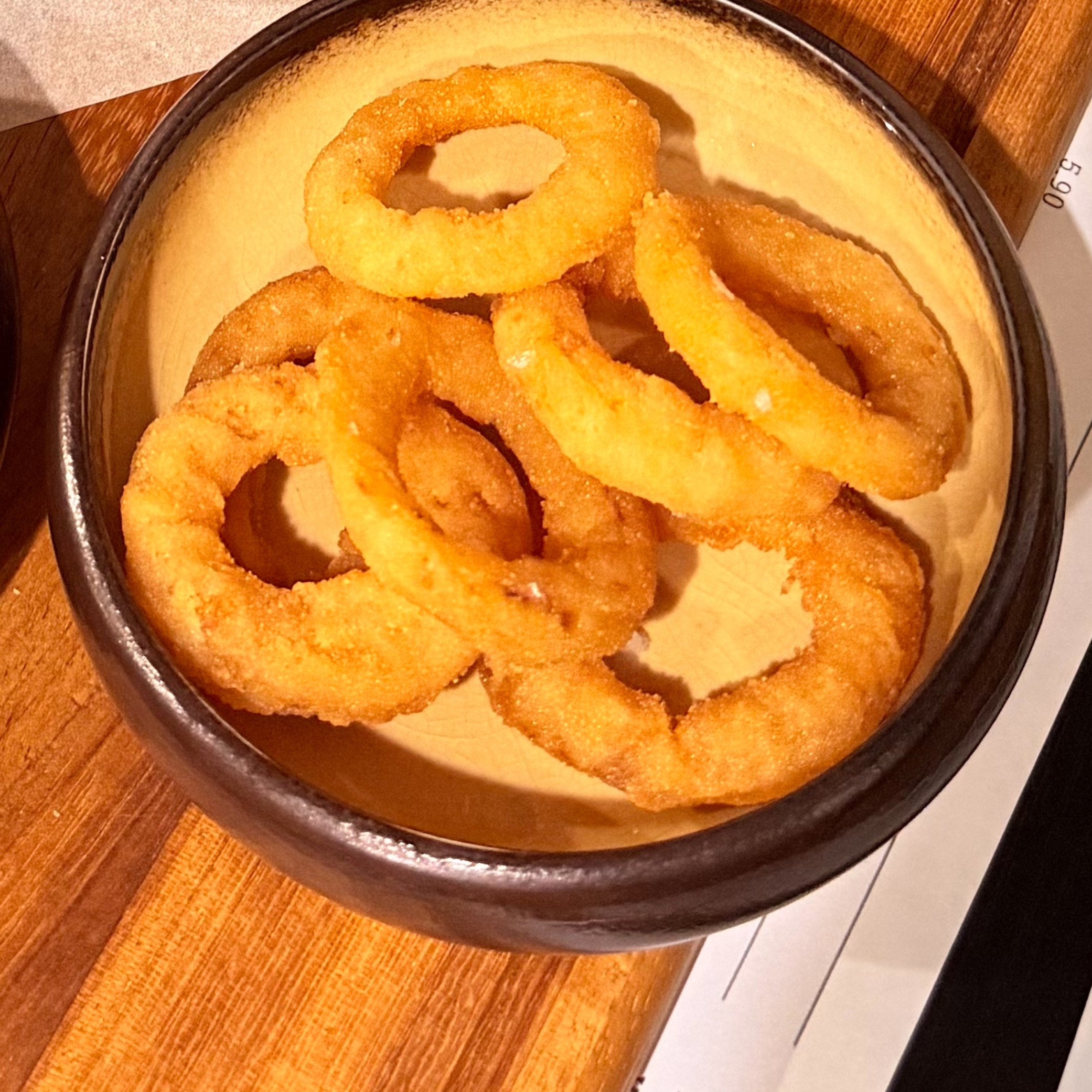 Golden fried onion rings in a brown bowl on a wooden table at Smoke House Košice next to a receipt showing 5.90