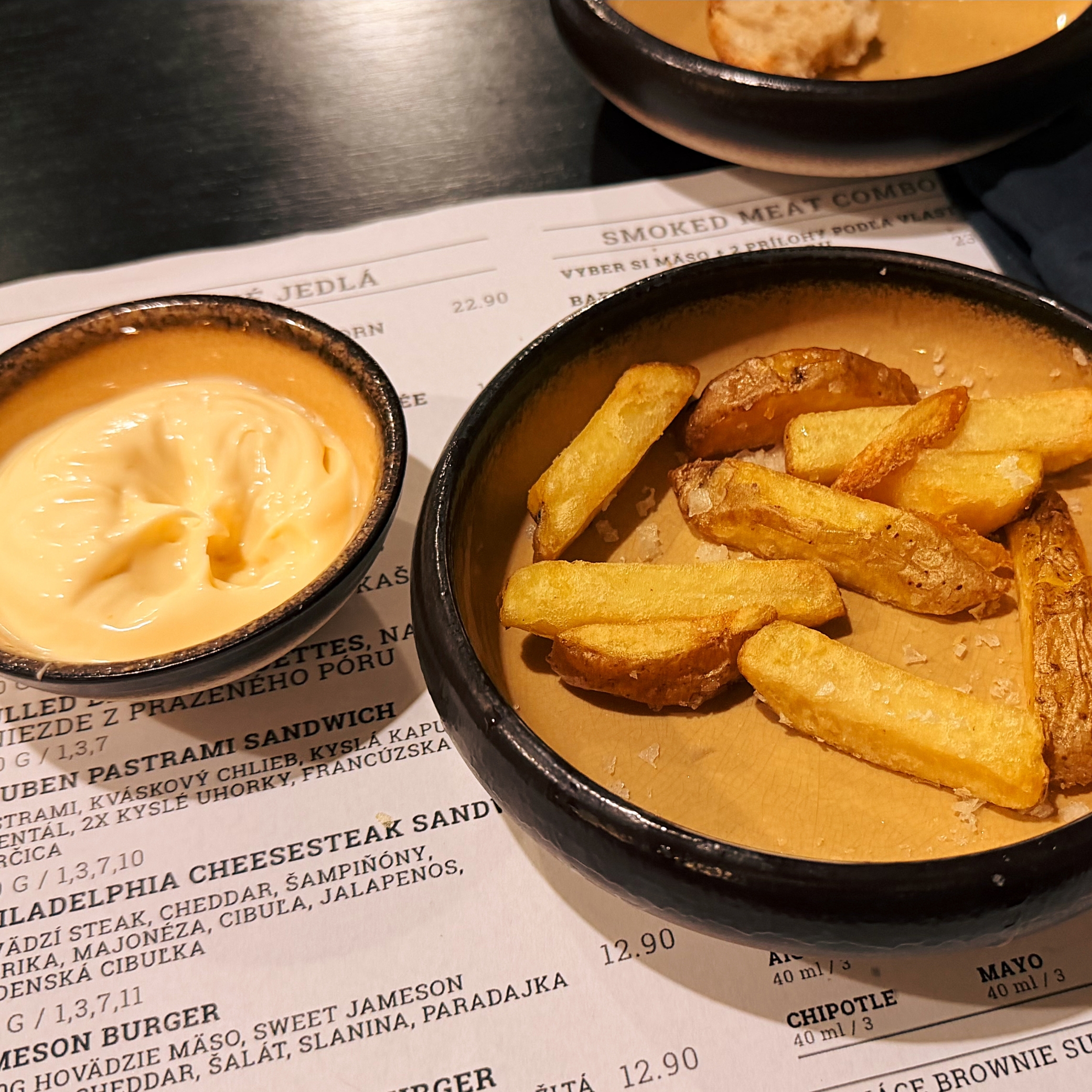 Bowls of thick fries and yellow sauce on a menu at Smoke House Košice showing the Smoked Meat Combo section