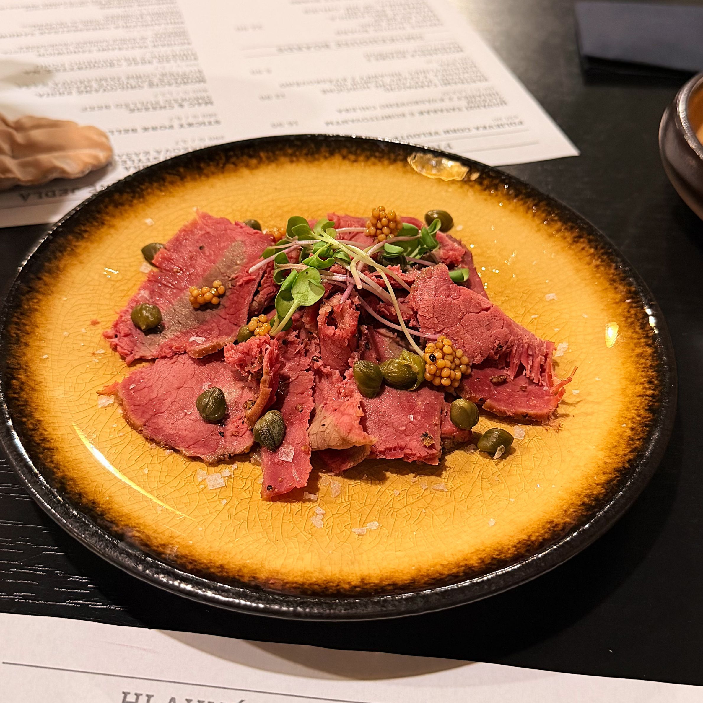 Slices of pastrami garnished with capers and mustard seeds on a yellow plate at Smoke House Košice