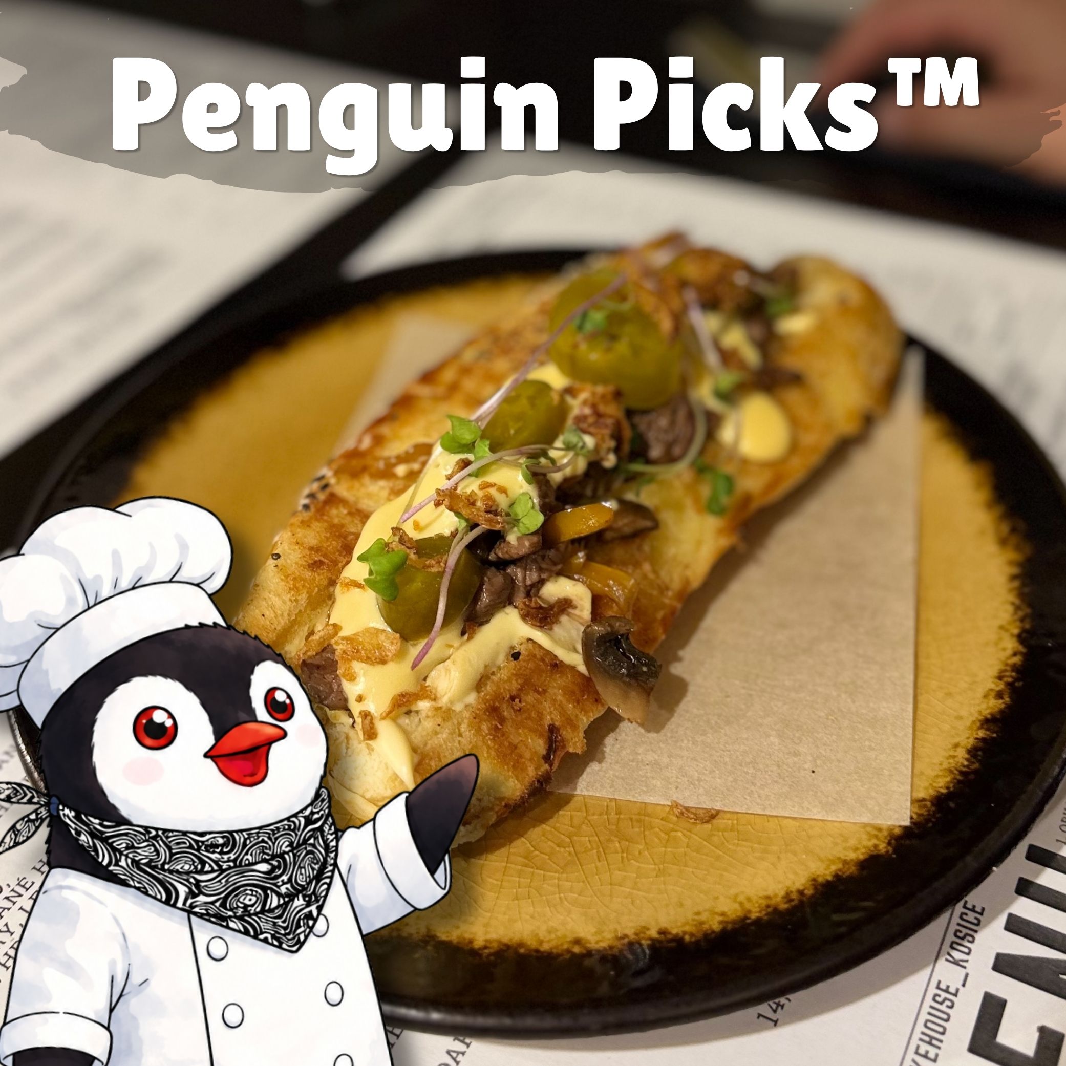A toasted roll topped with melted cheese mushrooms and pickles on a black plate with a cartoon penguin chef and text Penguin Picks