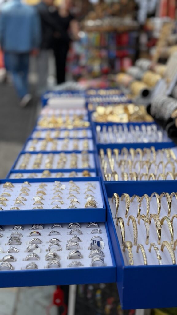 Blue trays filled with rows of gold and silver rings and bracelets displayed at a market stall in Prizren